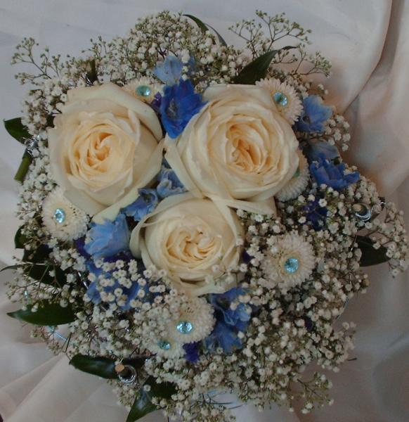 Creme roses, blue delphinium, white button mums and baby's breath, nestled in a blue and silver wire nest, accented with blue jewels and greenery