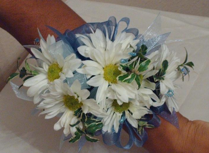 A simple corsage made of white daisies, greenery, and blue ribbon
