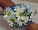 A simple corsage made of white daisies, greenery, and blue ribbon
